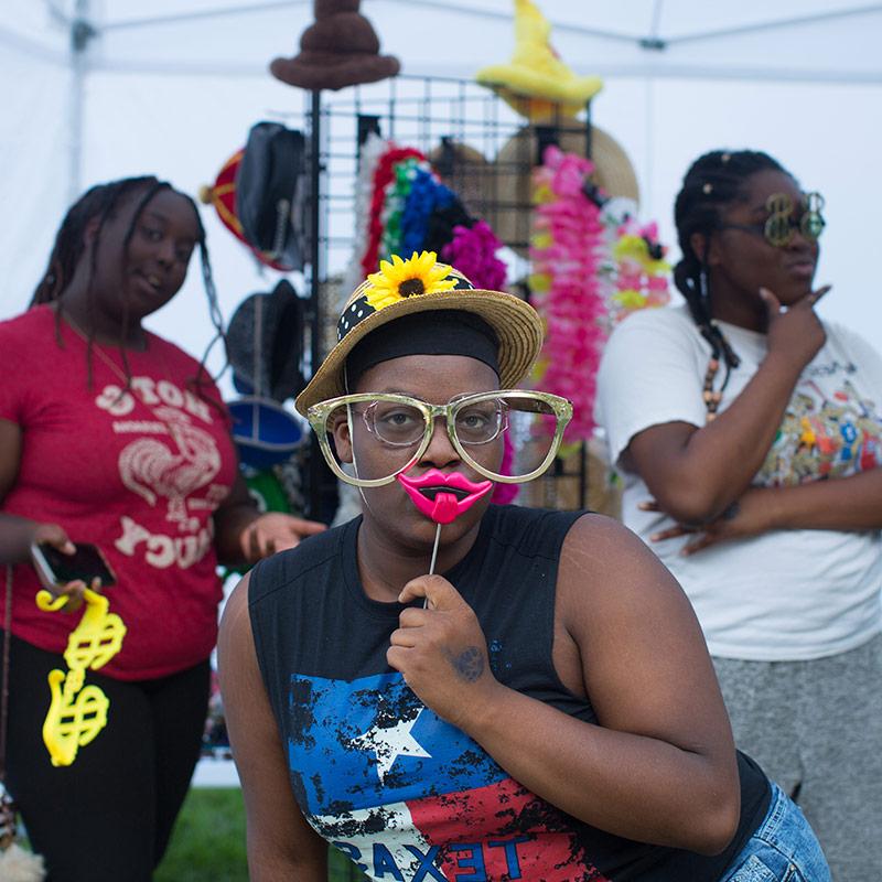 Three Drake University students posing with props at a photo booth outside on campus